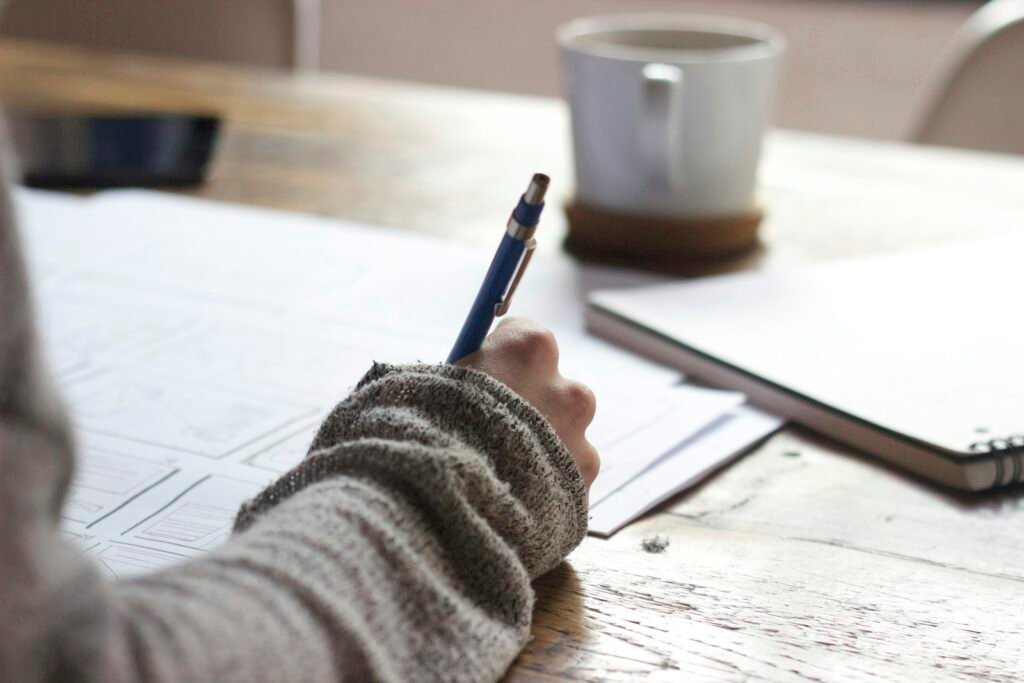 Student writing at a desk while reviewing academic work